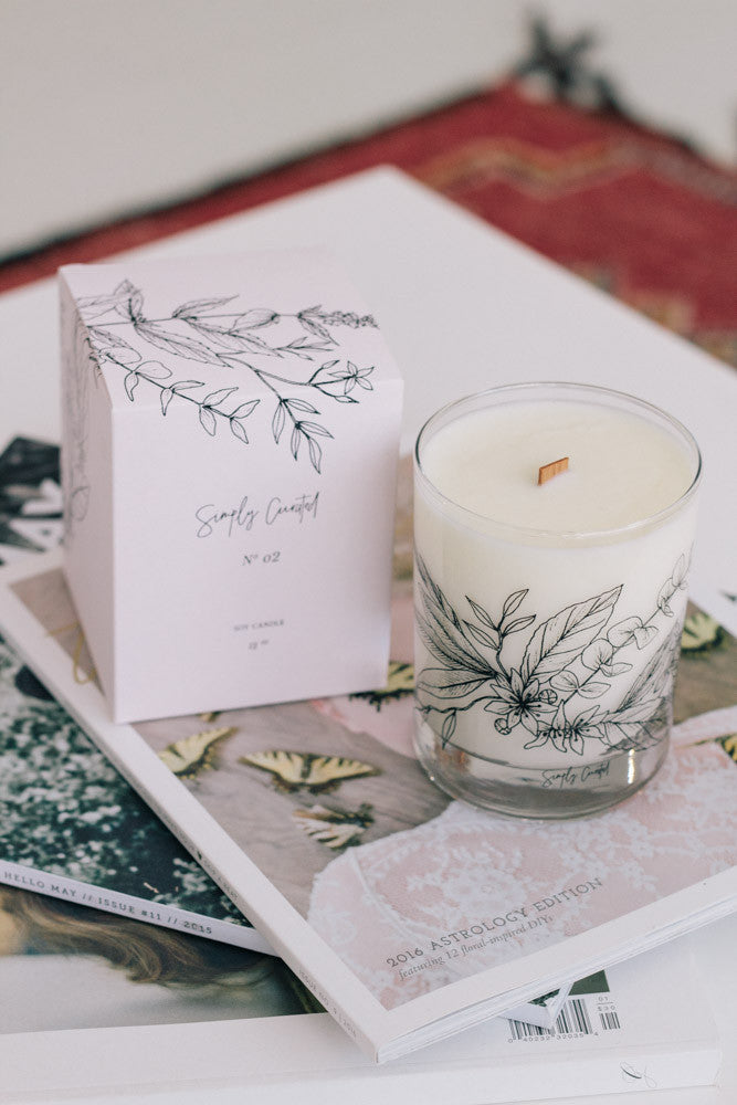 eucalyptus basil star jasmine soy candle with botanical illustration on the glass with a crackling wooden wick and a blush gift box on top of magazines