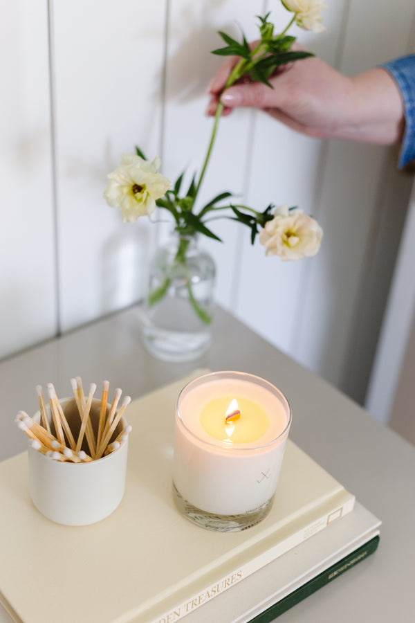 candle with wood wick burning styled on top of books with flowers in the background